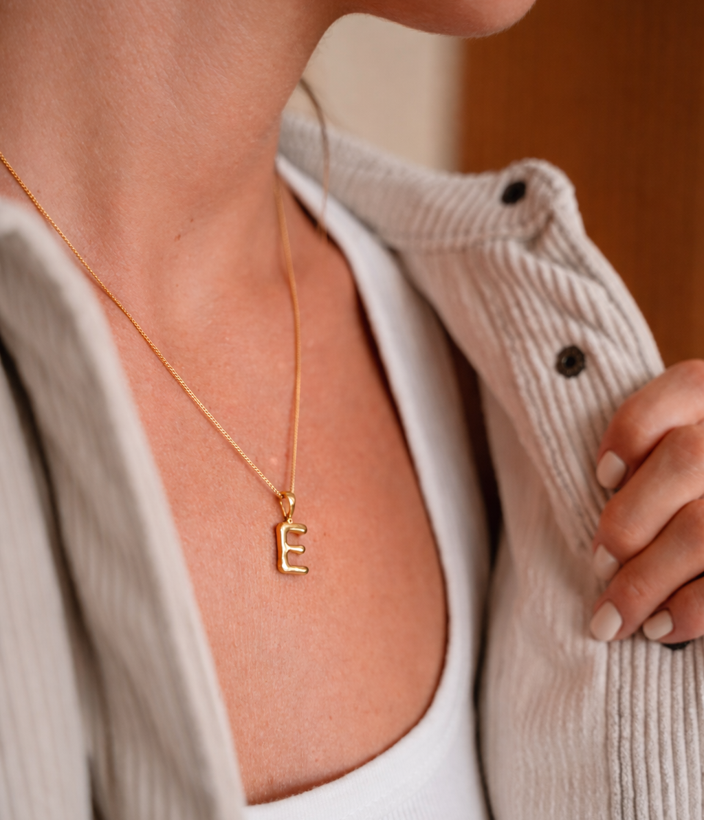 Goldener E Bubble Buchstaben Kette in gold mit weißem T Shirt und gebräunter Haut. Goldene Initialen Kette von VERLAN