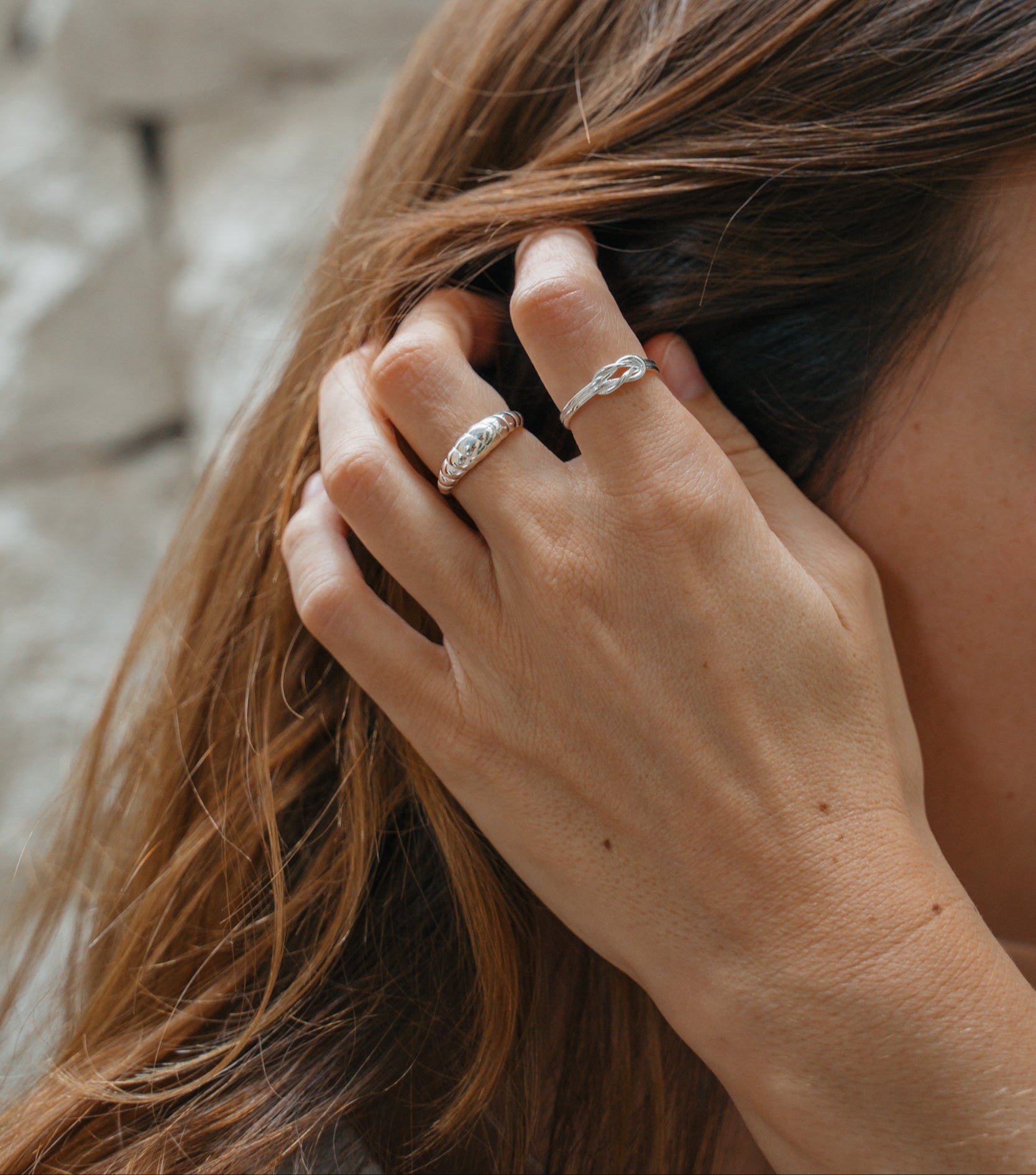 Silber ringe aus Bali an weiblichem Model. Croissant Ring und Knoten Ring aus Echtsilber, die wasserfest sind. Das Model fässt sich durch seine langen braunen Haare.