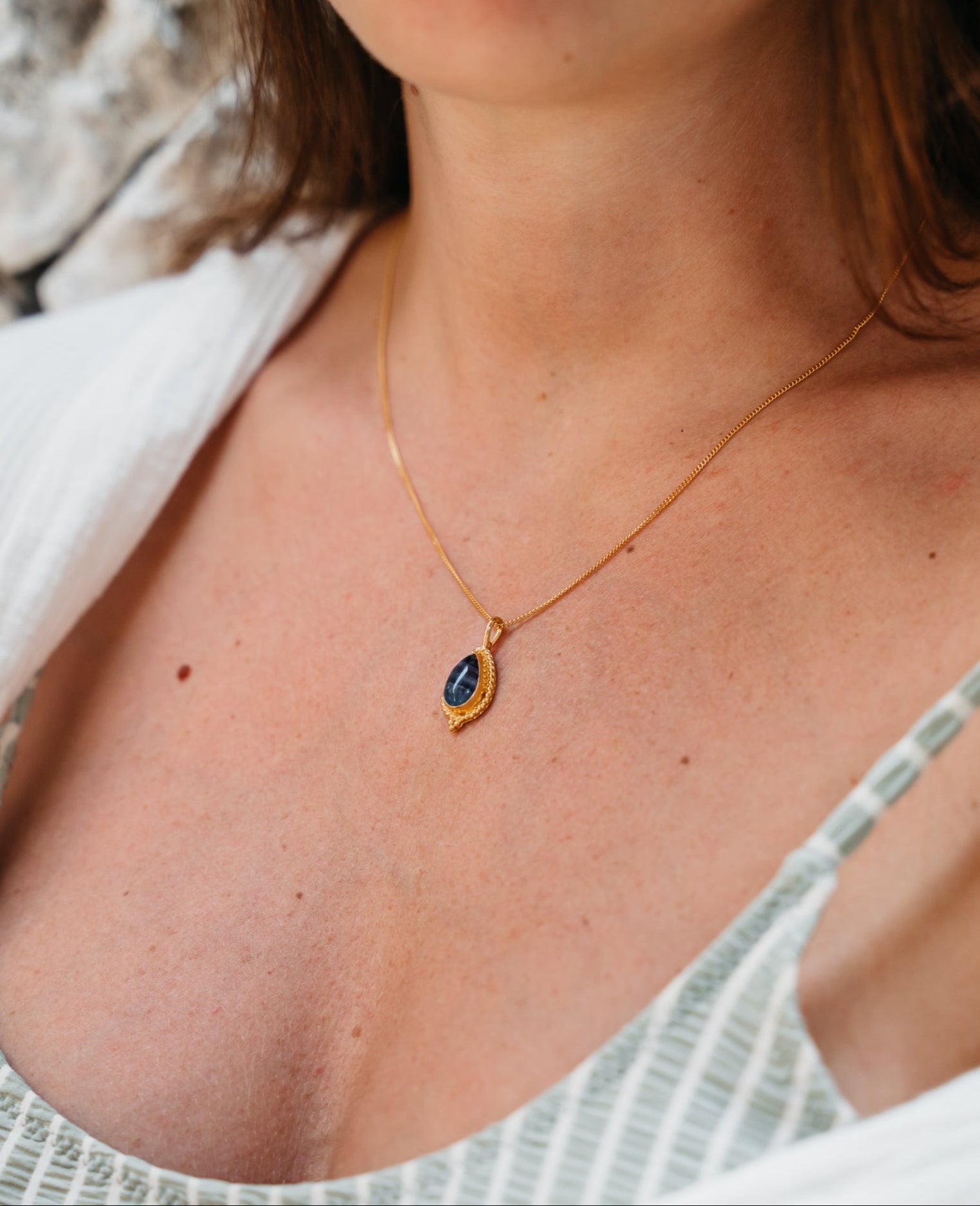 Goldene Kette mit Fluorit Stein im Boho Look von Verlan Jewellery. Das weibliche Model trägt die Kette einzeln und dazu eine weiße Bluse und ein türkis gestreiftes Oberteil.