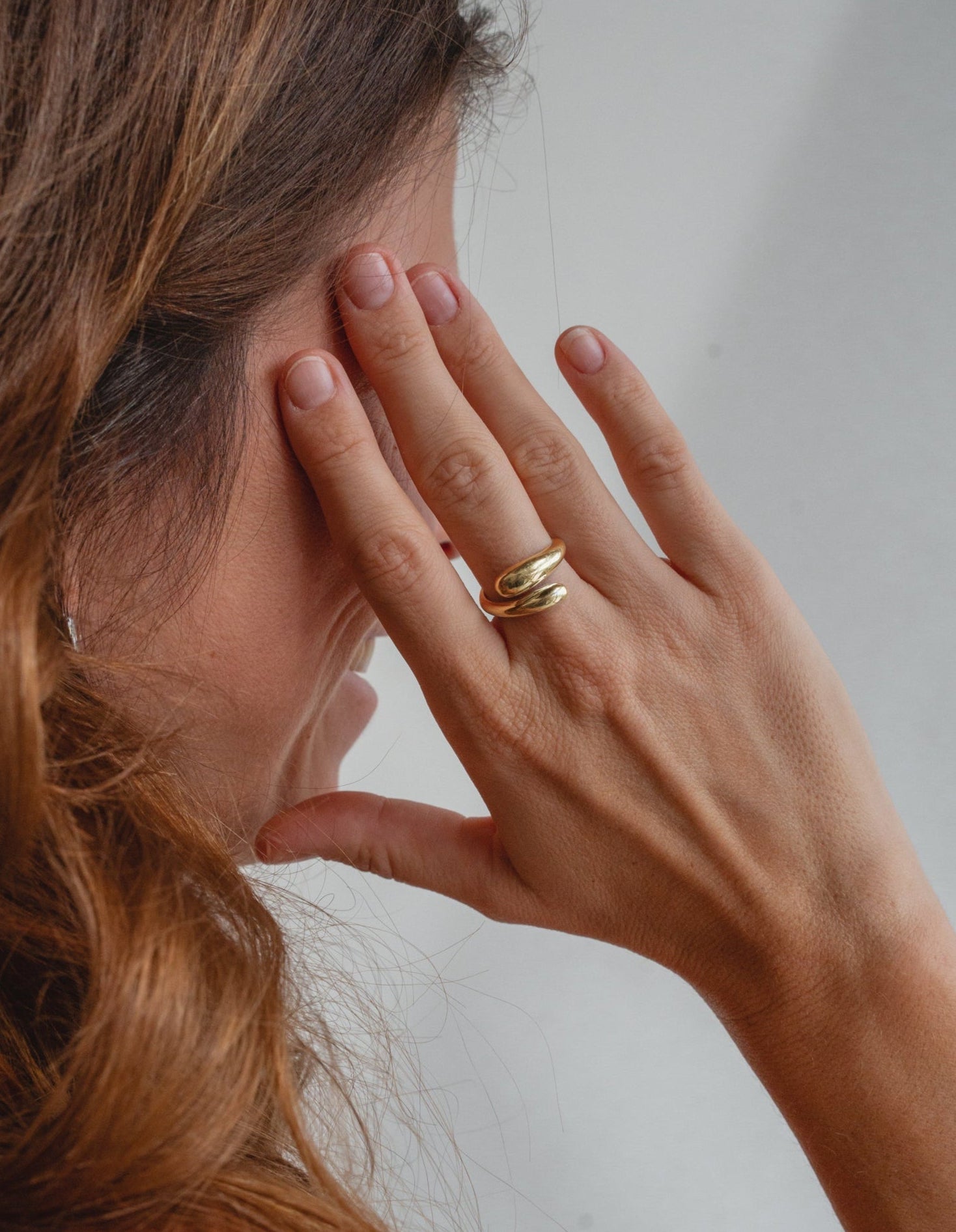 goldener Tropfen Ring in Schlangen Form auf gebräunter Haut. Das Model trägt auffälligen Gold Schmuck aus Bali