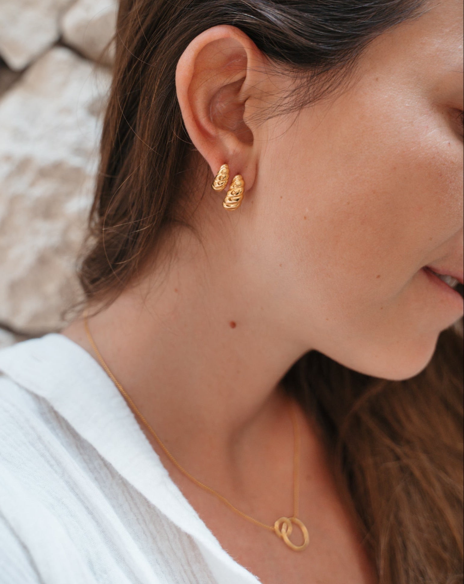 Croissant Ohrstecker in zwei verschiedenen Größen. Das weiblichen Model kombiniert zwei Ohrringe an einem Ohr. Goldener Bali Schmuck auf gebräunter Haut.