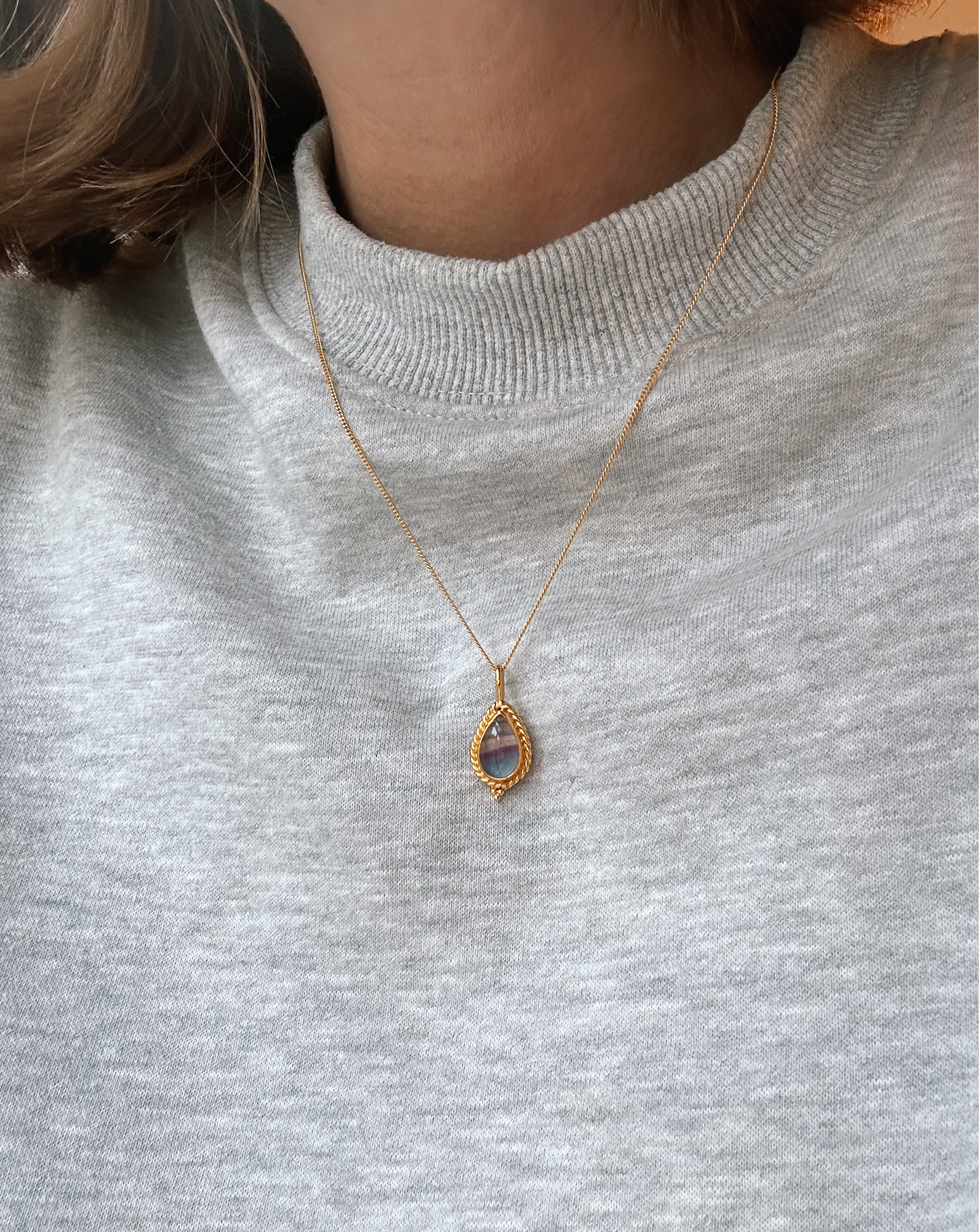 Goldene Kette mit Fluorit Stein im Boho Look von Verlan Jewellery. Model trägt grauen Pullover mit Kette darüber.