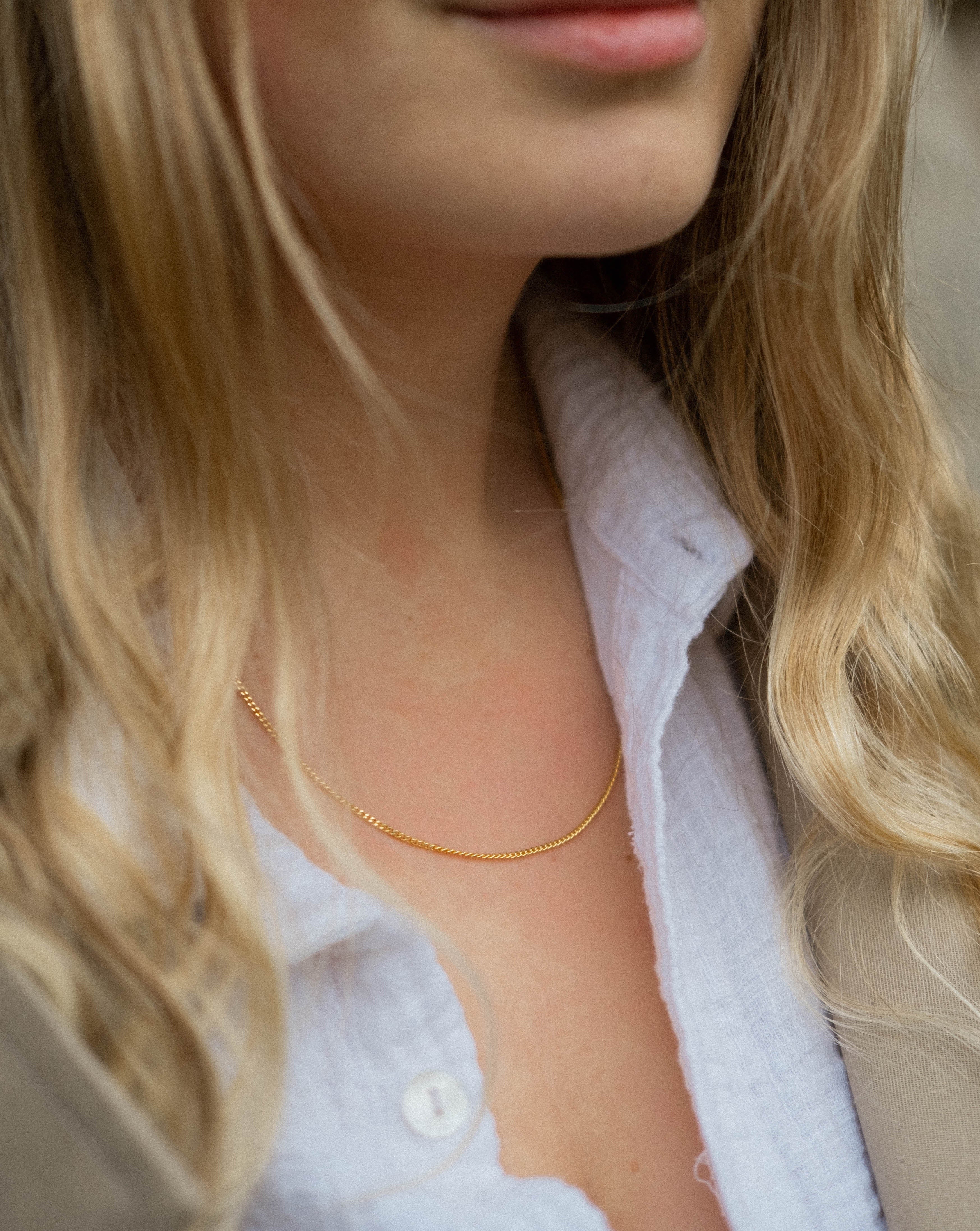Model trägt goldene Kette zu heller Bluse. Kette ohne Anhänger 